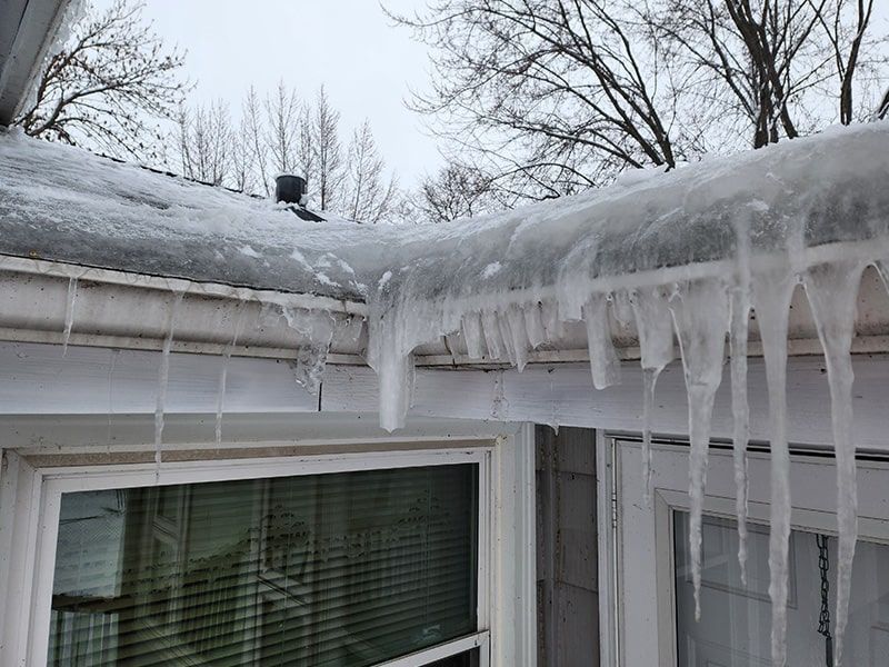Snow and ice buildup on a house roof and gutters, with icicles hanging down.