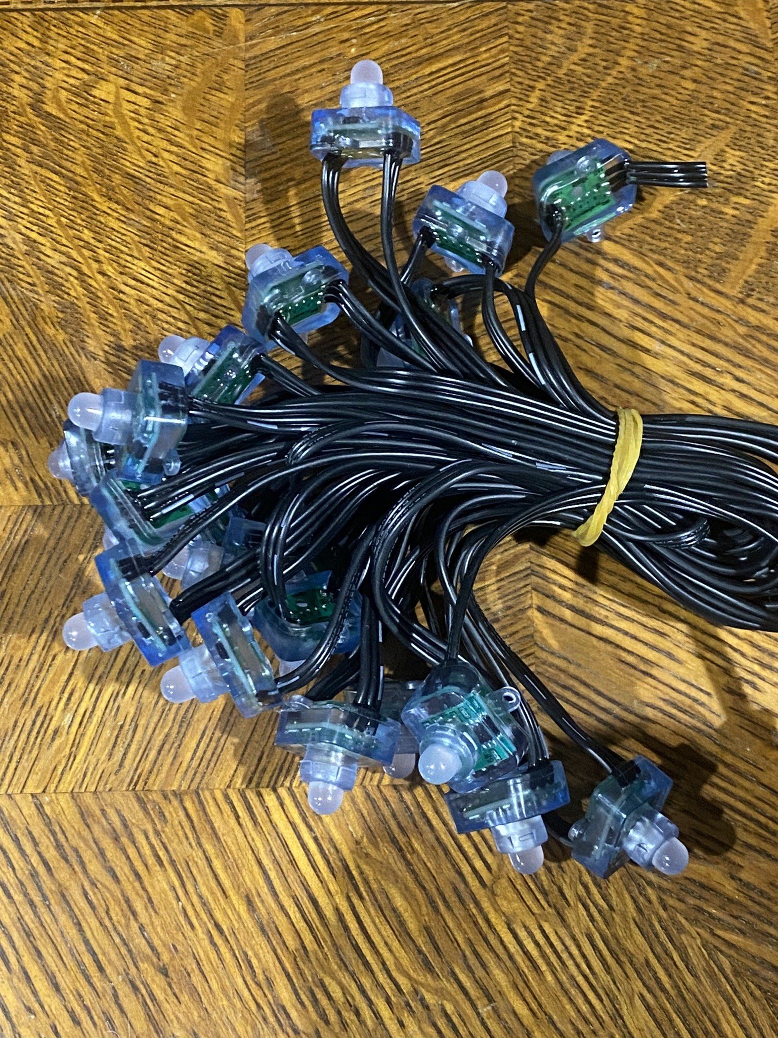 Bundle of black string lights with clear bulb covers and green connectors on a woven yellow surface