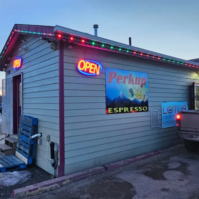 Small roadside espresso stand with neon OPEN sign and colorful lights at dusk