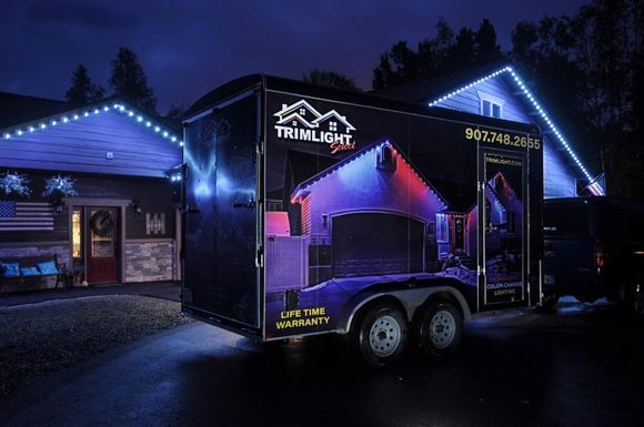 Branded trailer parked beside a house at night, lit by blue and purple accent lights