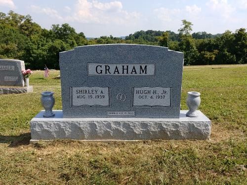 A gray granite headstone for the Graham family in a grassy cemetery with a forested background.