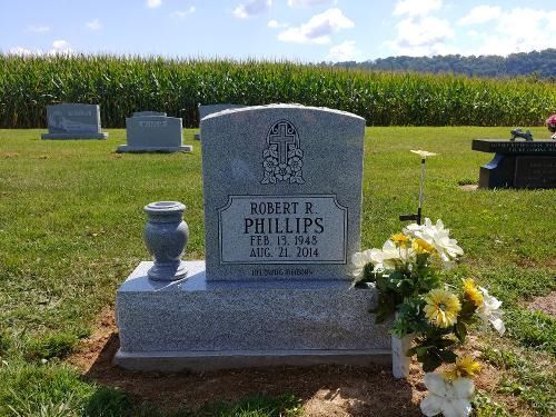 A grey granite tombstone for Robert R. Phillips in a grassy cemetery field with corn crops in the background.