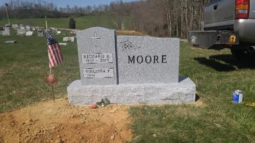 A granite headstone for the Moore family in a cemetery, featuring two names, a cross, and an American flag nearby.
