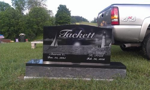 A black polished granite tombstone for the Tuckett family, featuring an etched lighthouse, sailboat, and sun in a cemetery.