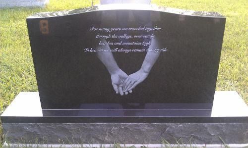 A black granite headstone features an etching of two hands clasped together with a poem inscribed above them.