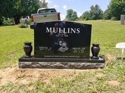 A black granite double headstone for the Mullins family in a grassy cemetery, featuring an etched portrait and text.