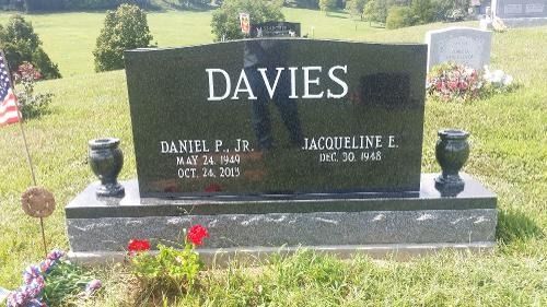 A black granite double headstone for the Davies family in a cemetery, featuring dates for Daniel P. Jr. and Jacqueline L.