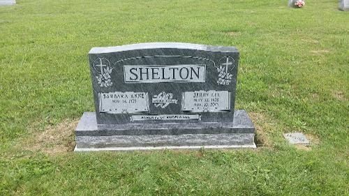 A grey granite gravestone for the Shelton family, centered in a grassy cemetery field.