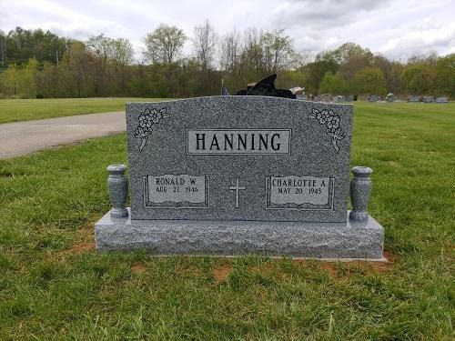 A gray granite headstone for the Hanning family, inscribed with two names and dates, set in a grassy cemetery.