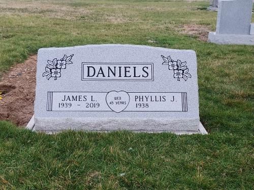 A granite grave marker for the Daniels family, with names James L. (1939–2019) and Phyllis J. (1938) on a grass lawn.