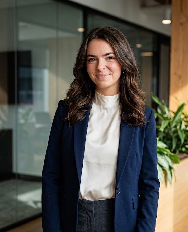 Woman in a navy blazer stands smiling in a modern office hallway