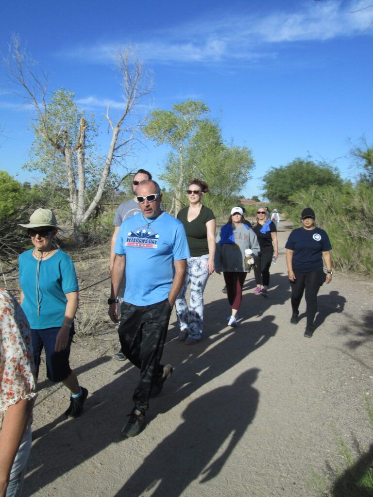 People walking together on a sunny desert trail under a clear blue sky.