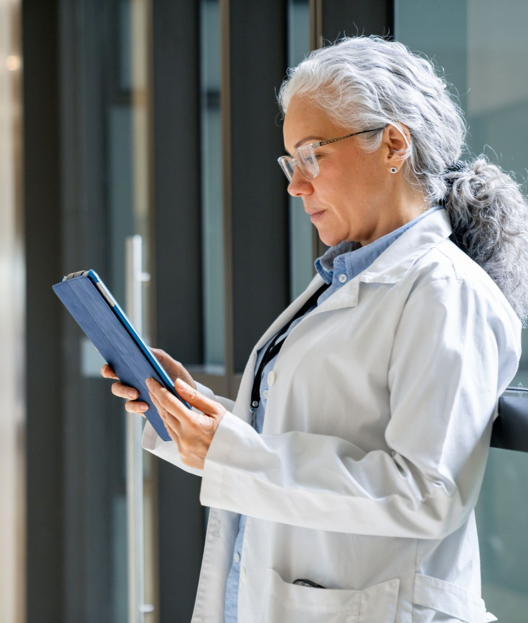 Scientist in a white lab coat reading a blue tablet in a bright hallway