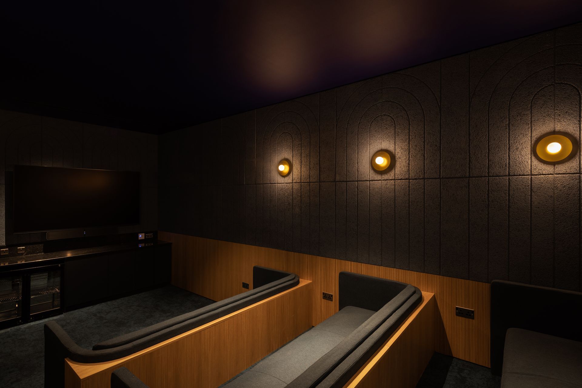 Dim, modern lounge with wooden booths, dark walls, and warm wall sconces.