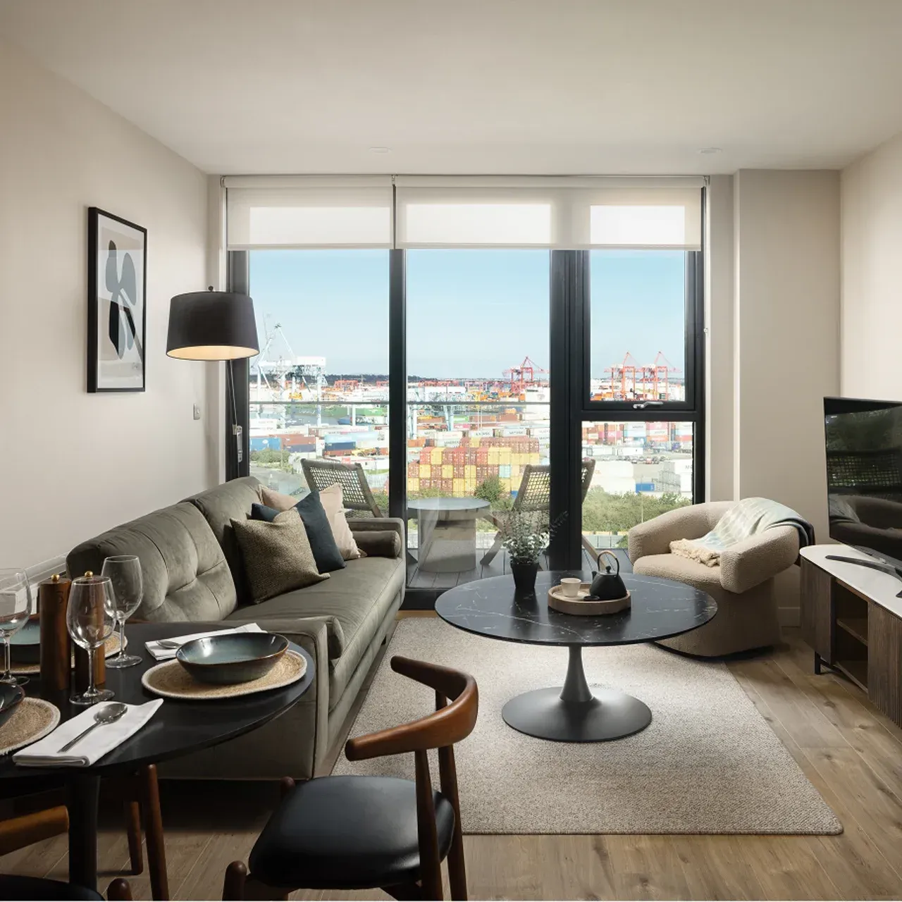 Modern living room with city view, gray sofa, round black table, and large windows.