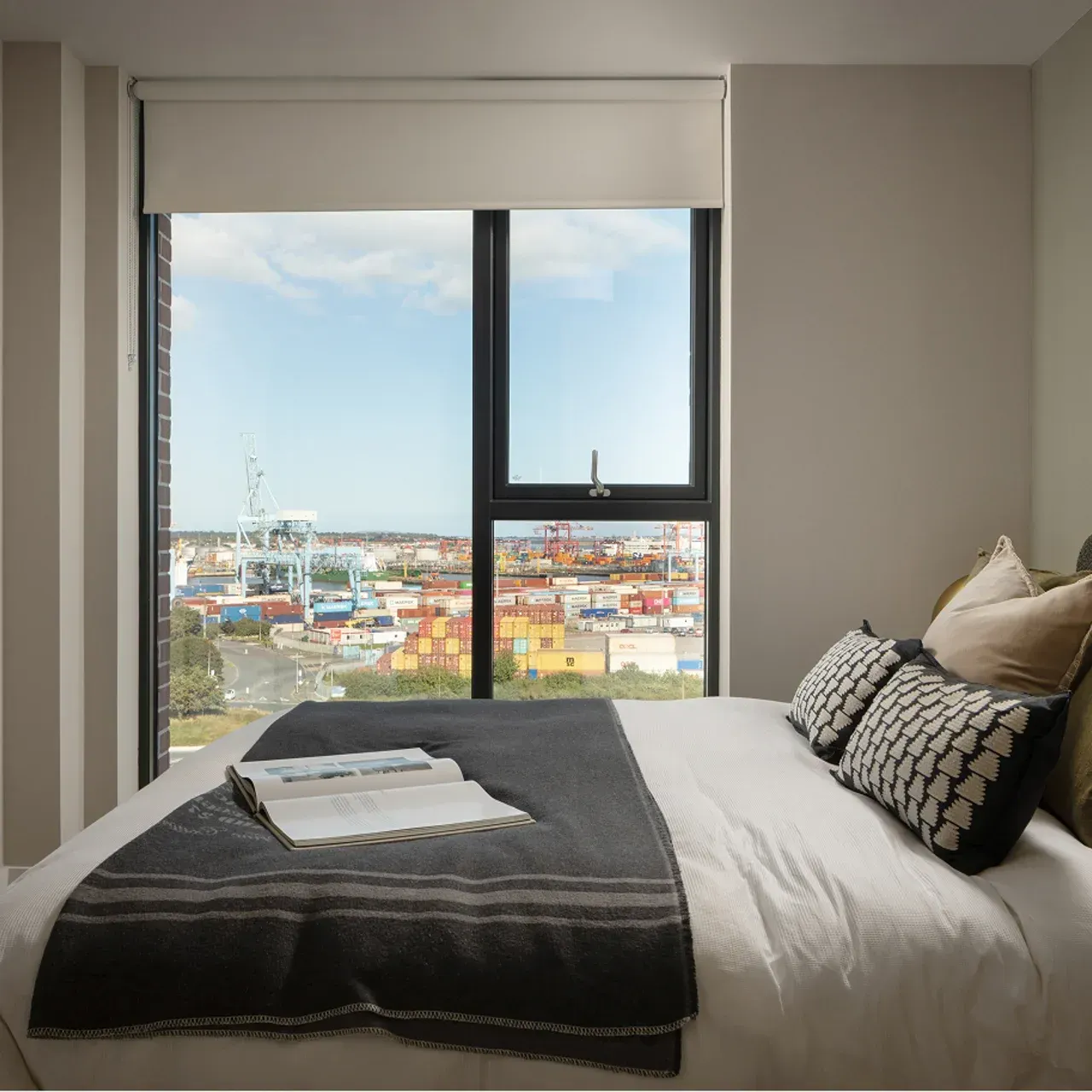 Modern bedroom with bed by large window overlooking a city and harbor.