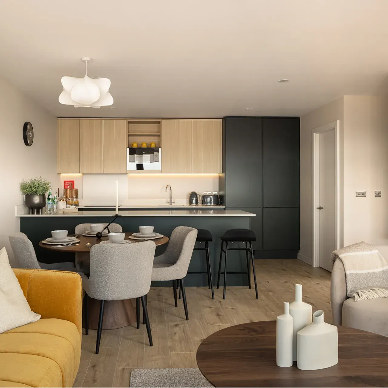 Modern open-plan kitchen and dining room with light wood cabinets, black island, and yellow sofa in foreground