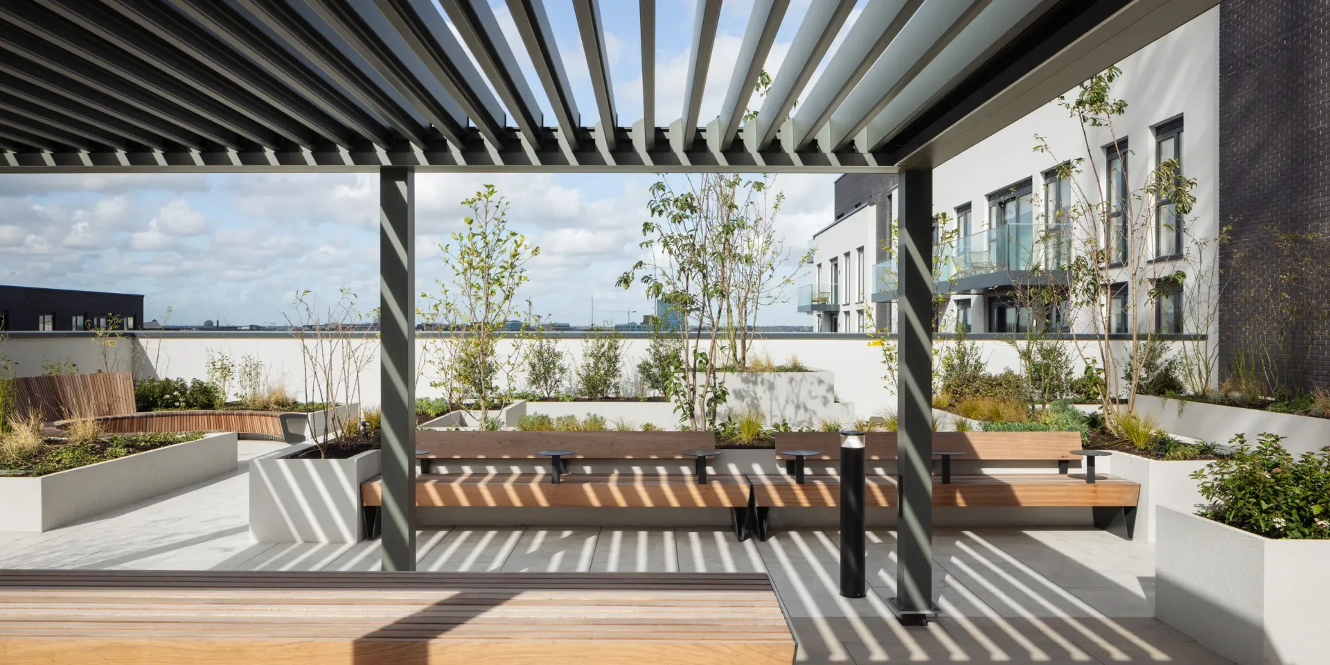 Modern rooftop terrace with pergola, benches, planters, and city apartment buildings