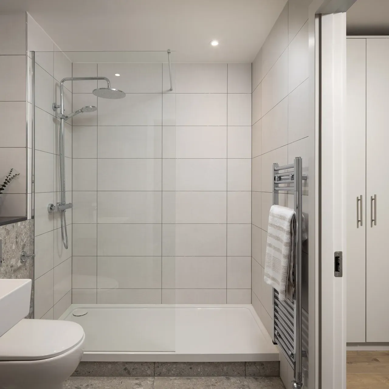 Modern white tiled bathroom with a glass shower, towel rack, and sink partially visible
