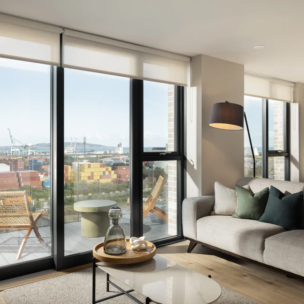 Bright modern living room with large windows, city view, gray sofa, coffee table, and floor lamp