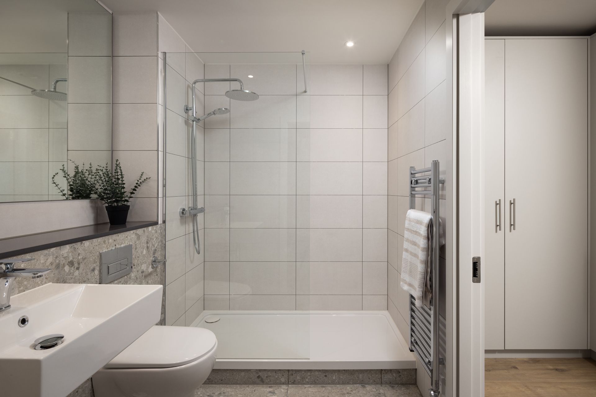 Modern bathroom with glass shower, white sink, toilet, and built-in wardrobe