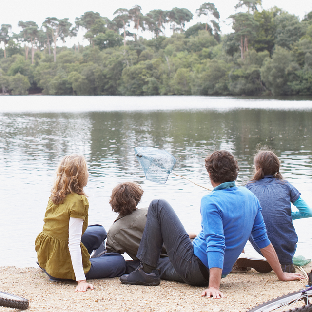 Five people sit by a lake, looking at a splash in the water with trees across the shore.