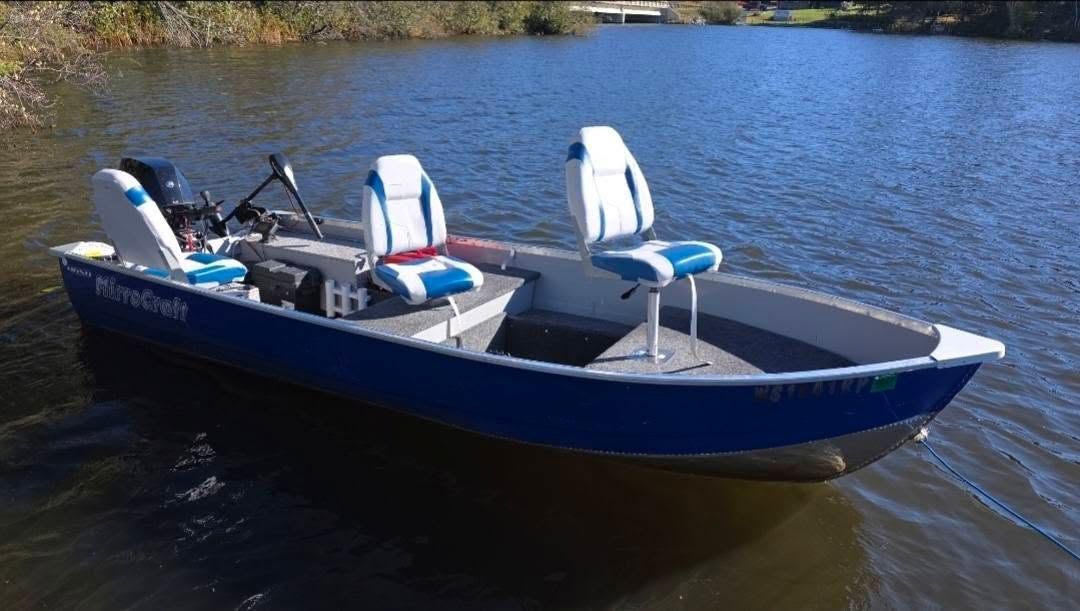 Blue pontoon boat with canopy floating on a calm lake near a wooded shore