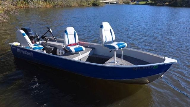 Blue pontoon boat with canopy floating on a calm lake near a wooded shore