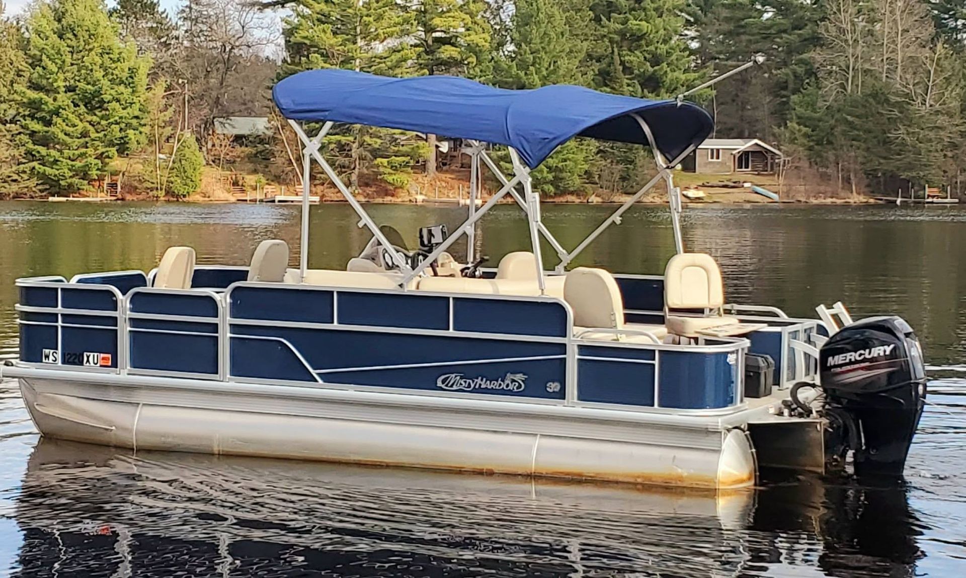 Pontoon boat with black canopy docked in calm water on a sunny day