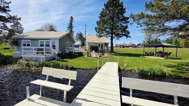 Lakeside cabin with dock, benches, picnic shelter, and trees under a clear blue sky