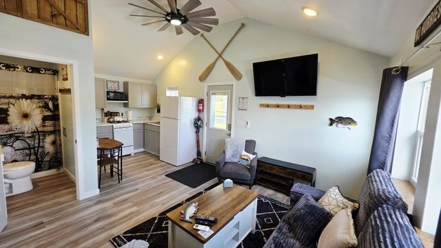 Bright living room with sofa, wall-mounted TV, ceiling fan, striped rug, and open dining area