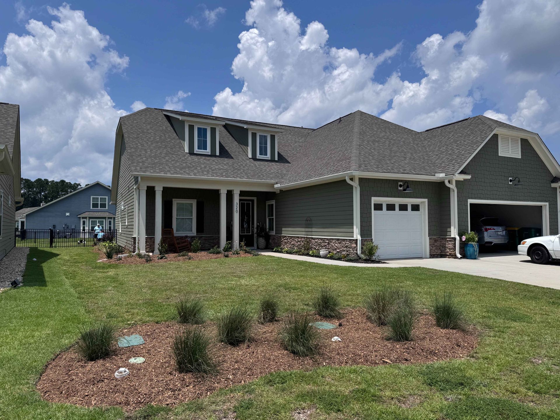 Green house with two-car garage, dormer windows, and well-manicured front lawn with shrubbery.
