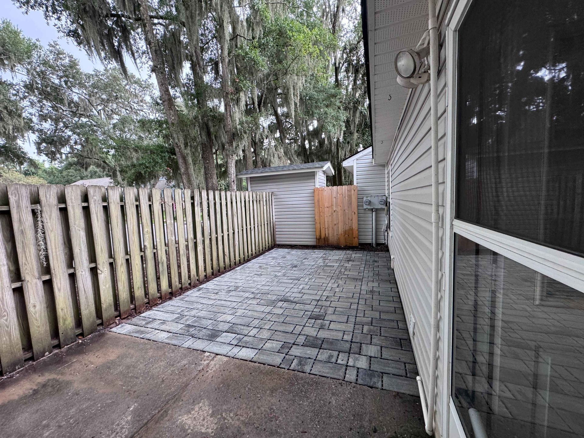 Small backyard patio with brick pavers, wooden fence, and shed.