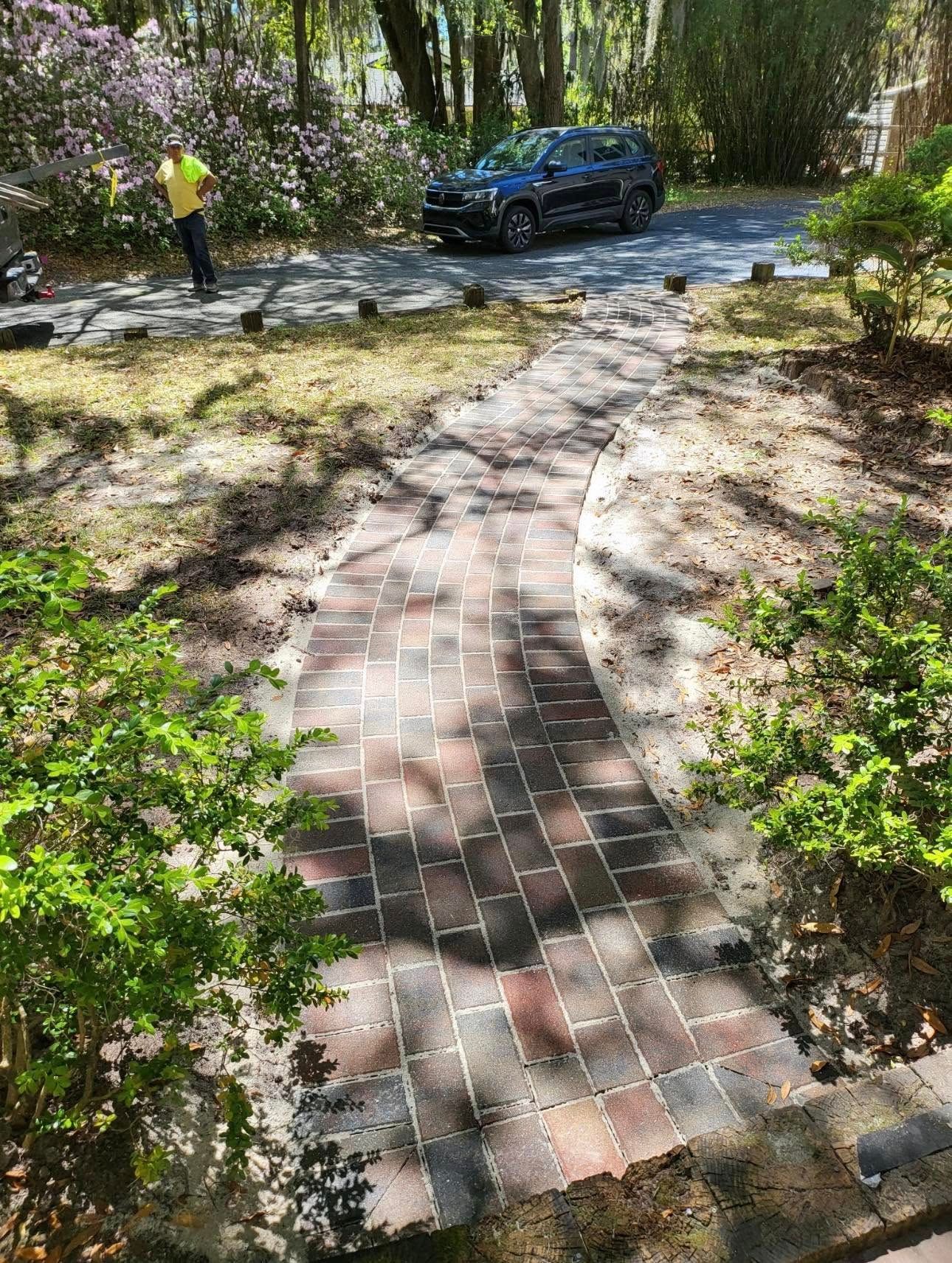 A man is working on a brick walkway in a yard.