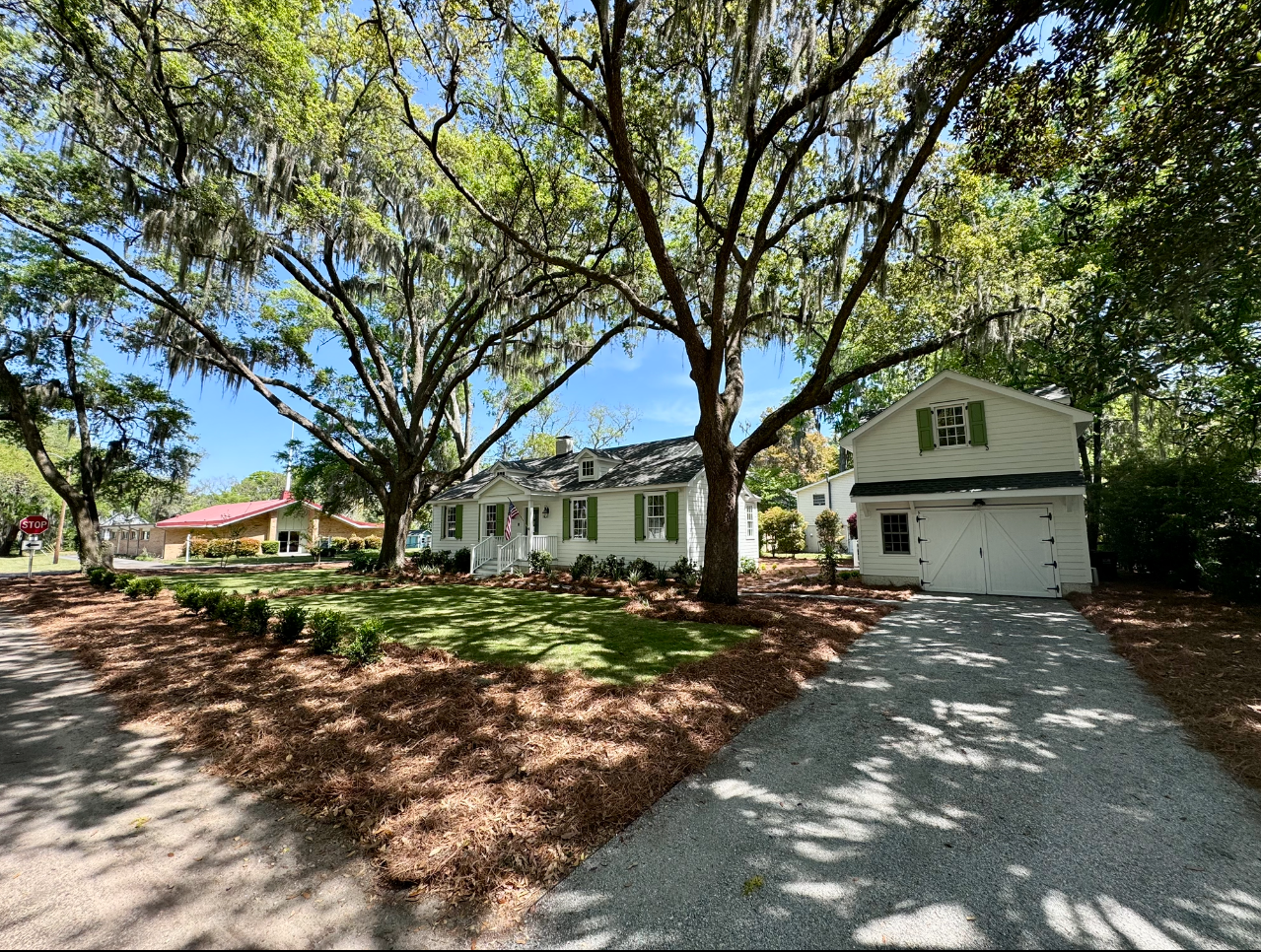 A white house with a driveway and trees in front of it.