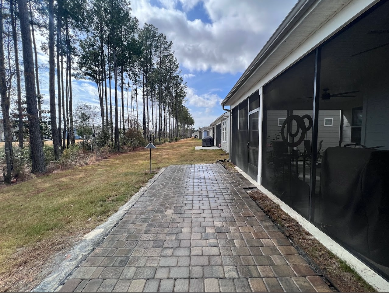 A brick walkway leading to a screened in porch with trees in the background.