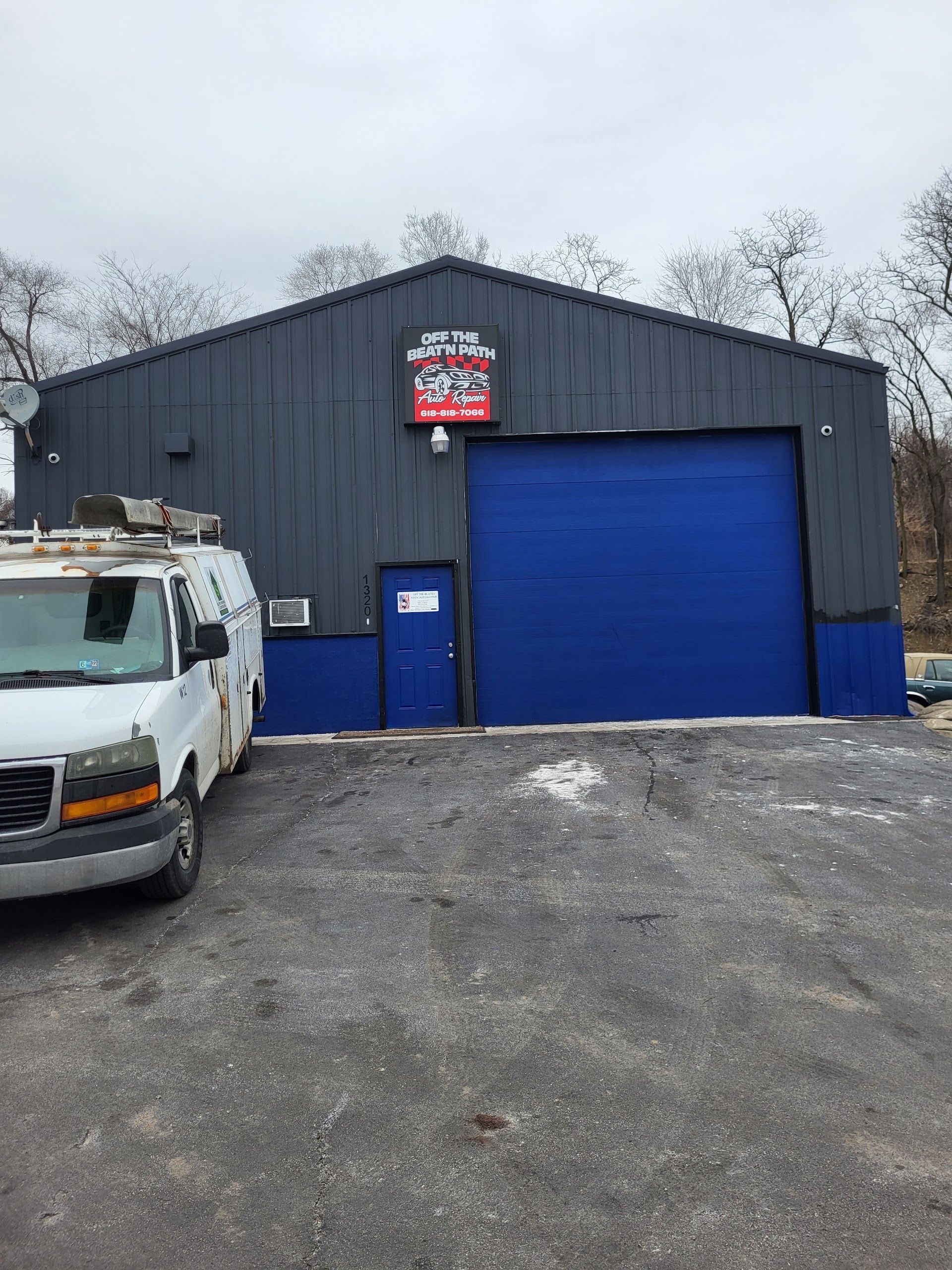 Small gray garage building with a bright blue door, a white van parked beside it, and a gravel lot | Off The Beaten Path Automotive LLC