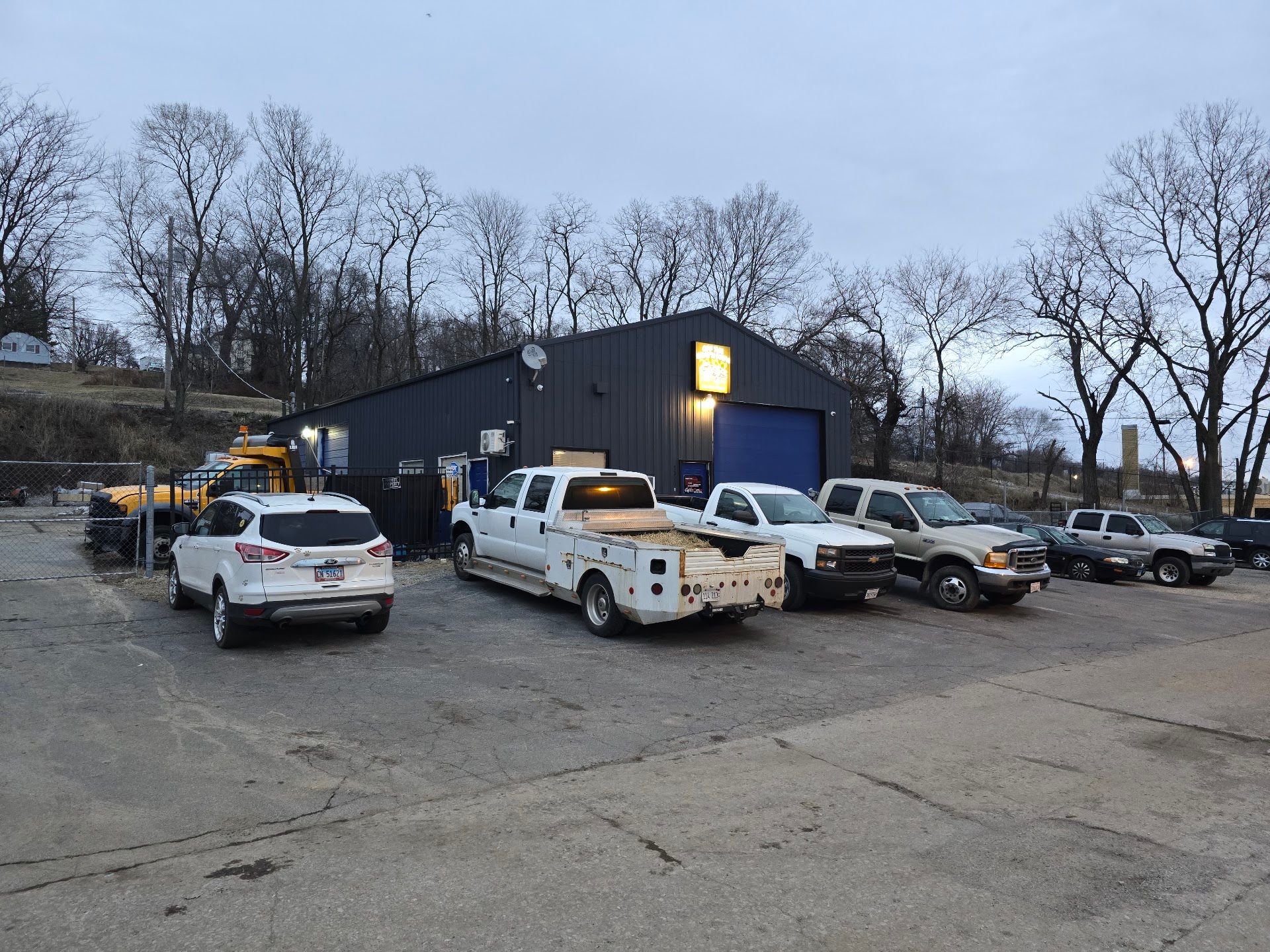 Several utility trucks and SUVs parked outside a dark blue building at dusk | Off The Beaten Path Automotive LLC