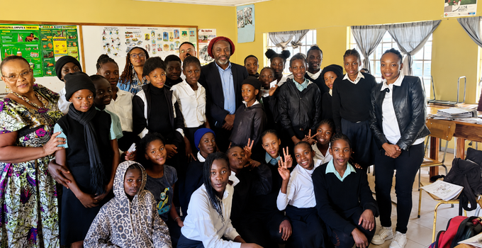 Groupe d'élèves et d'enseignants posant dans une salle de classe, vêtus de tenues formelles et souriants.