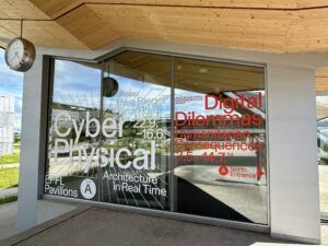 Vitrine vitrée avec texte d'exposition cyber-physique blanc et rouge sous un auvent en bois