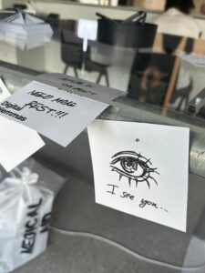 Carte manuscrite avec un dessin d'œil et les mots « Je te vois… » sur une table d'exposition en verre