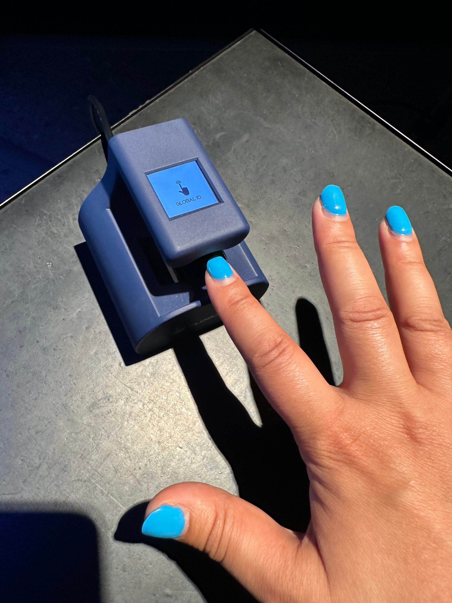 Une main aux ongles bleu vif appuie sur un bouton bleu d'un appareil sombre à l'extérieur.
