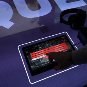Main touchant une tablette sur une table d'affichage éclairée en violet avec des éléments d'interface rouges et noirs