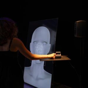 Une personne se penche vers un écran transparent lumineux dans une pièce sombre.
