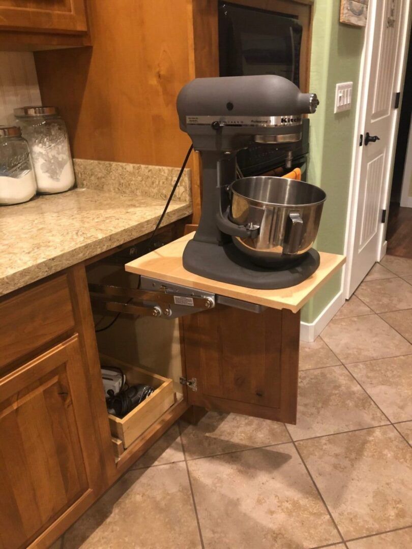 Kitchen cabinet with a pull-out shelf holding a gray KitchenAid mixer.