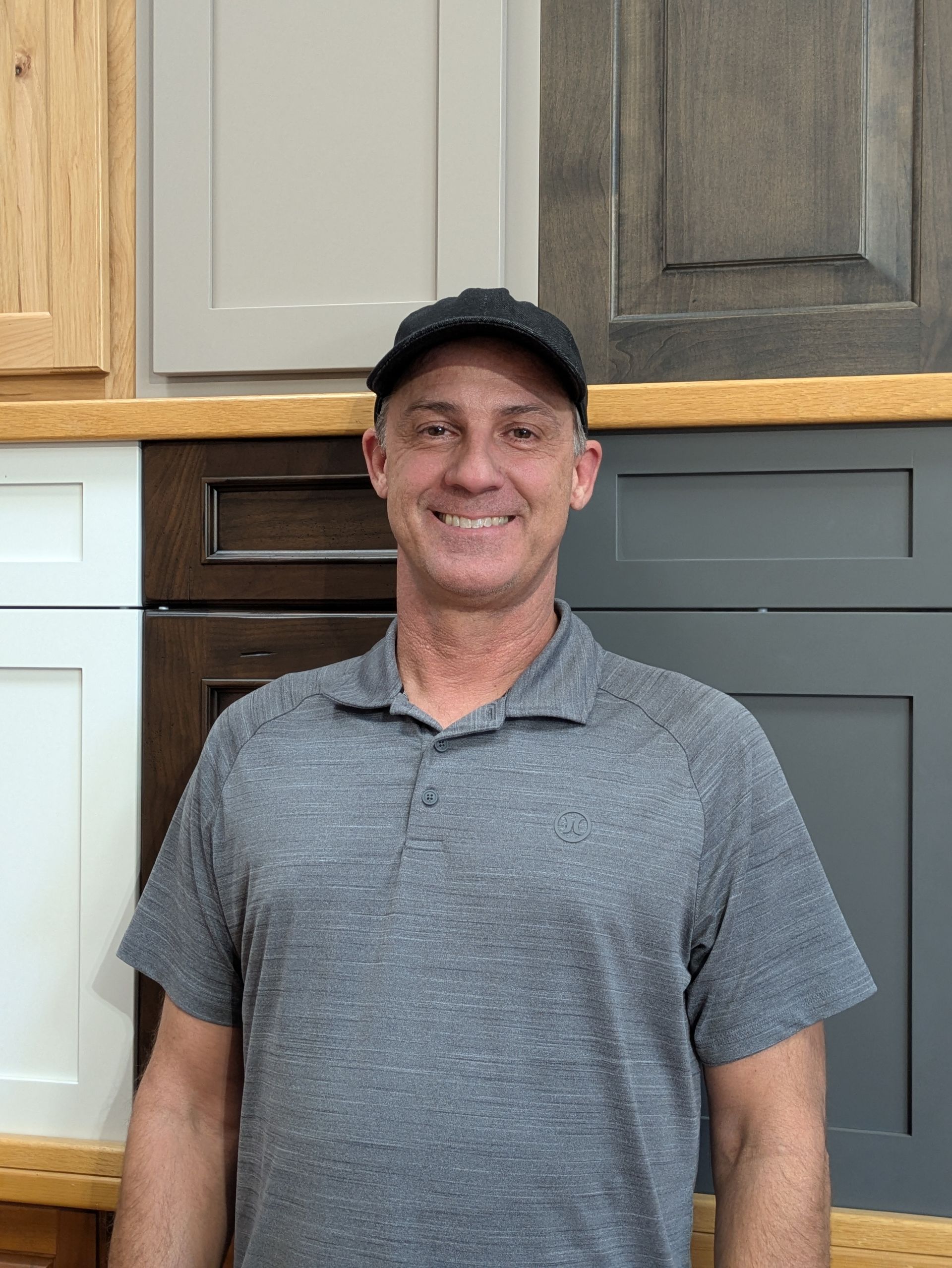 Man in gray shirt and baseball cap smiles in front of cabinet door samples.