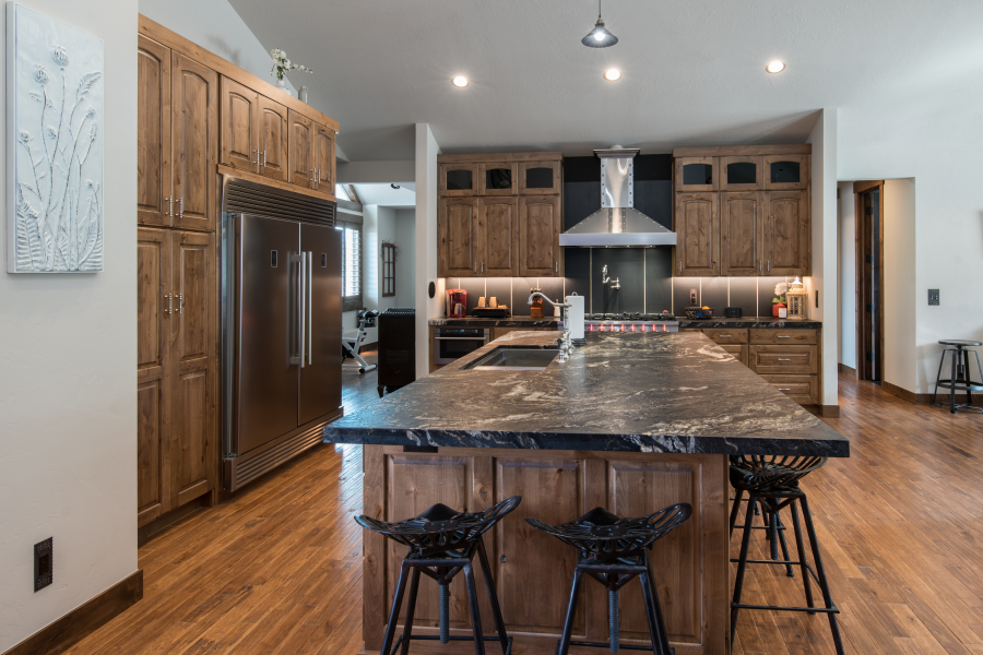 Wooden kitchen with a large island, stainless steel appliances, and dark countertops.