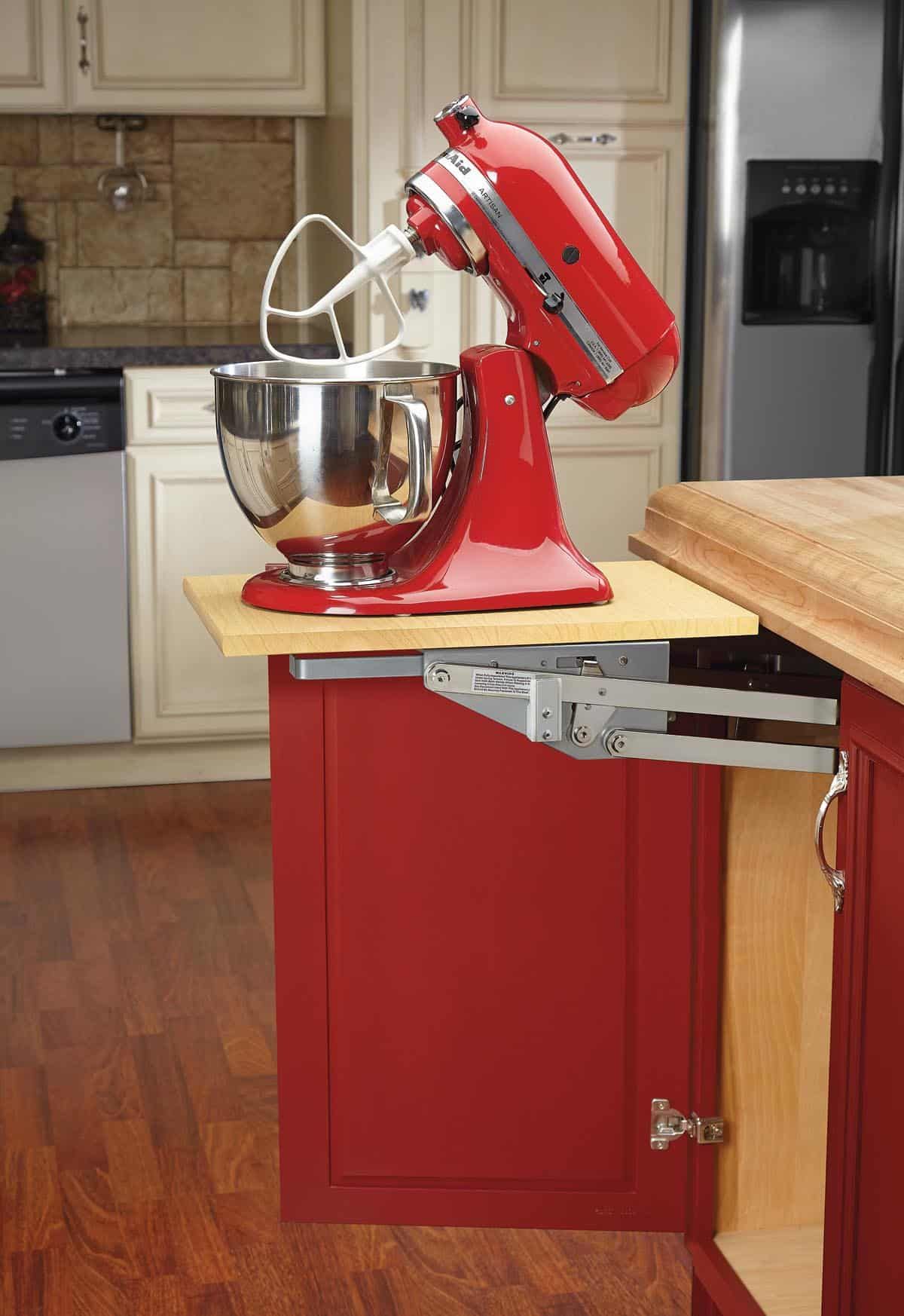 Red KitchenAid mixer on a pull-out shelf in a red cabinet. Stainless steel bowl, wooden countertop.