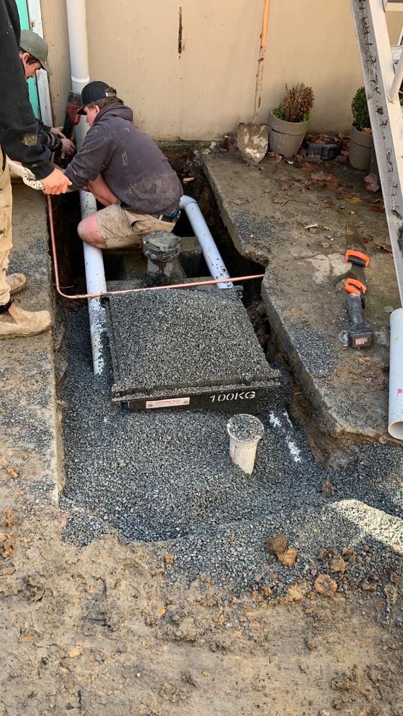 Worker installing gravel drain trench beside a beige wall and patio area