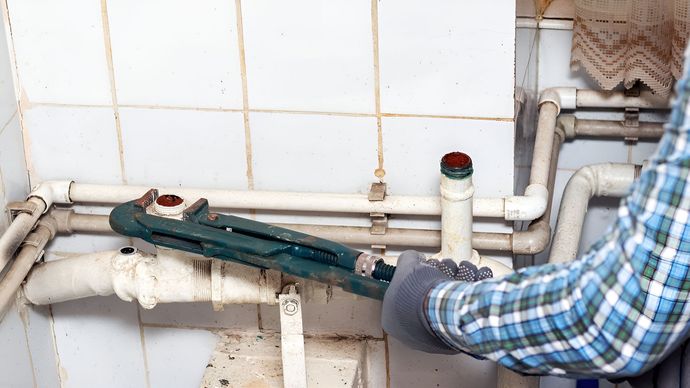 Person using a pipe wrench to repair plumbing under a tiled sink basin